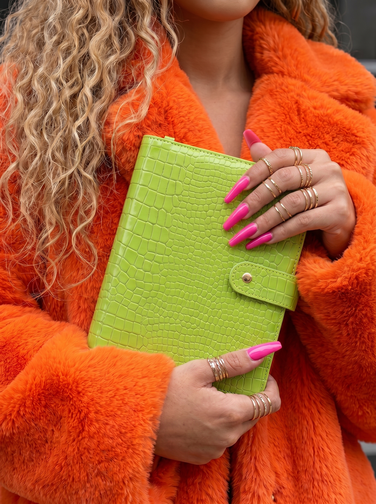 Person wearing an orange coat holding a green croc a5 planner with pink nail polish.